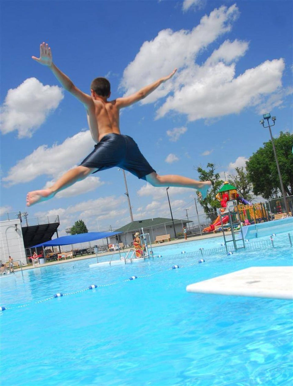 Kid jumping into a public pool on a bright day.